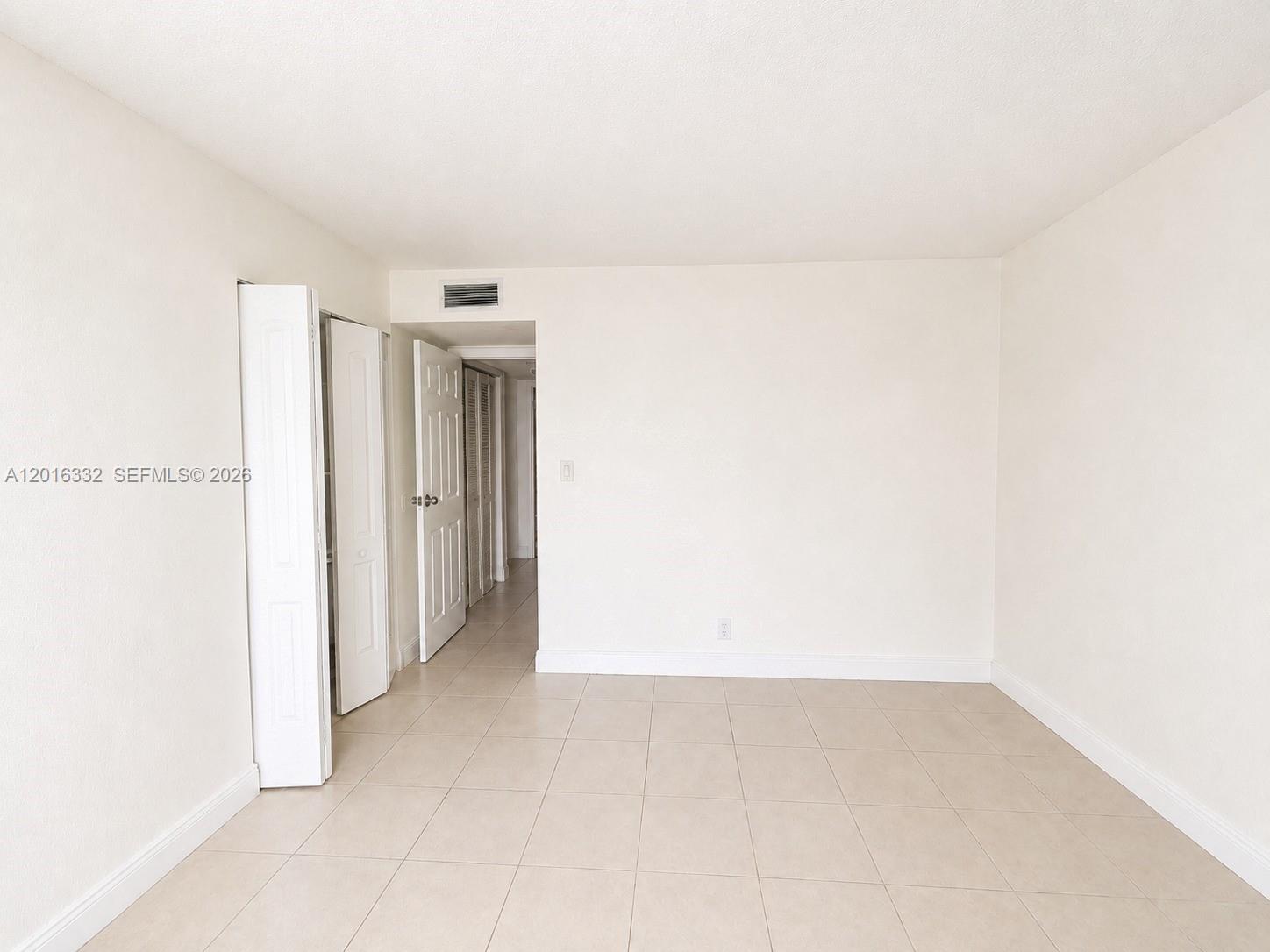 An empty room features beige tile flooring, white walls, and a closet with bifold doors — 17911 NW 68th Ave # M201, Hialeah FL 33015, HIALEAH, FL