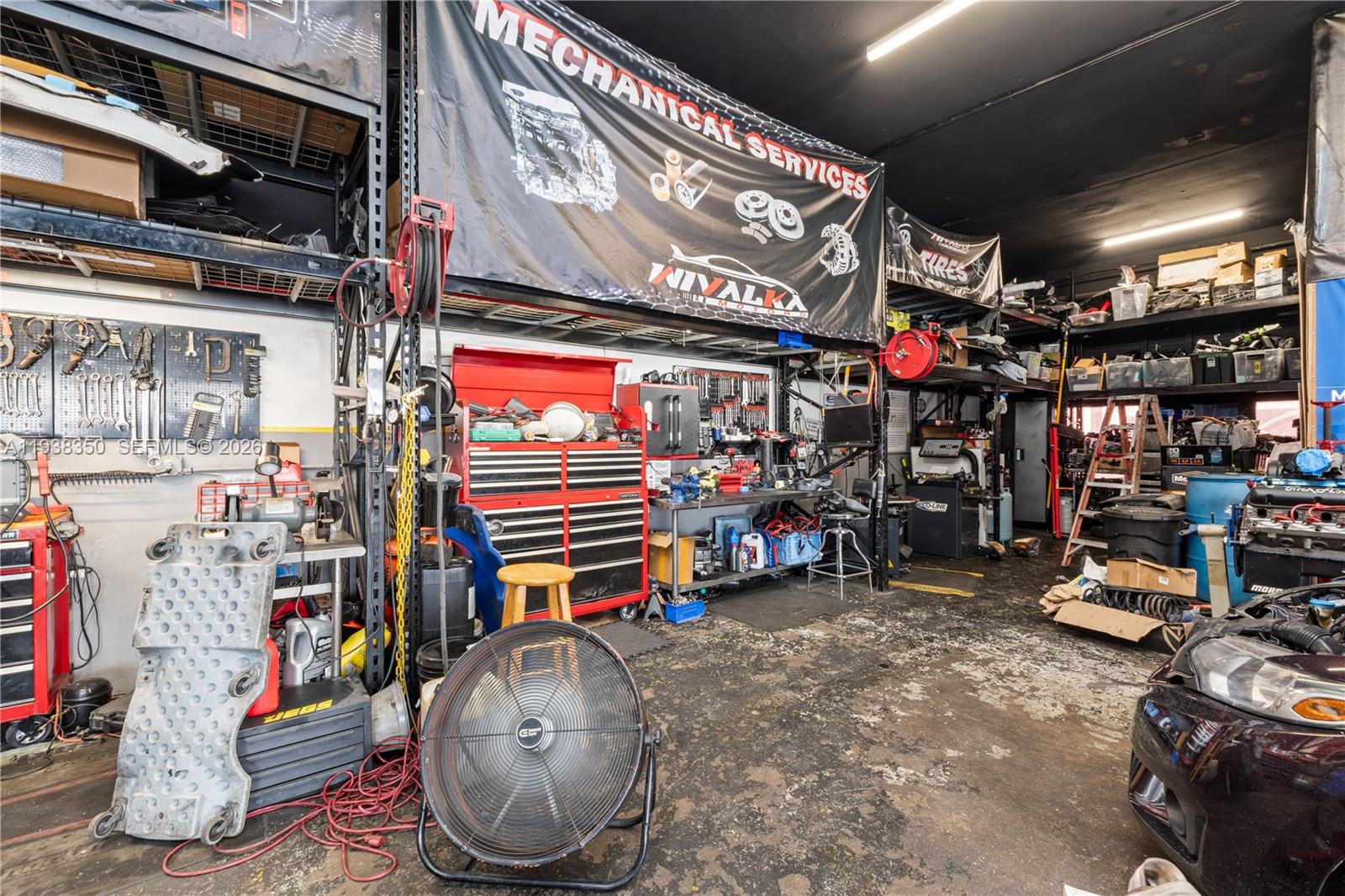 A cluttered automotive repair shop features workbenches, tool chests, equipment, and a large overhead banner — 4350 NW 32nd Ave, Miami FL 33142, MIAMI, FL
