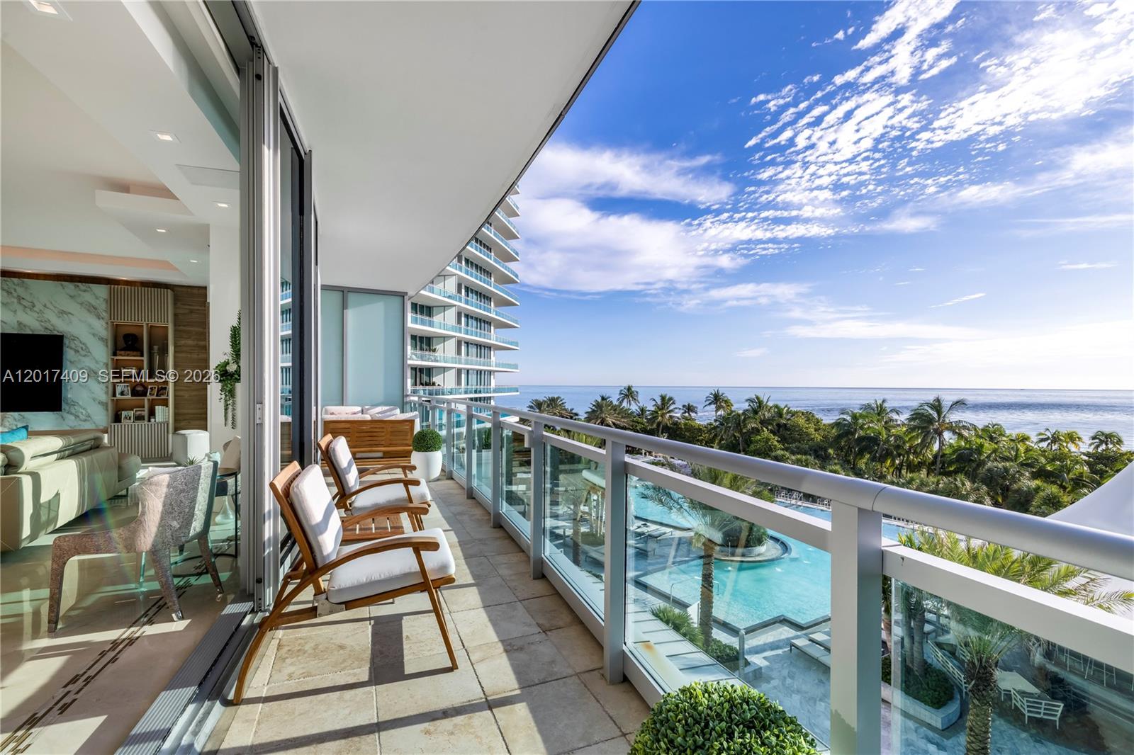 A balcony with wooden chairs overlooks a swimming pool, palm trees, and the ocean — 10295 Collins Ave # 301, Bal Harbour FL 33154, BAL HARBOUR, FL