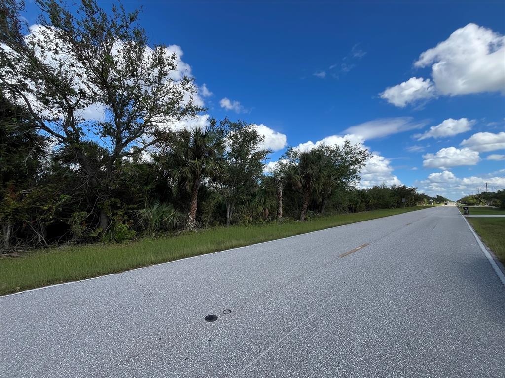 A paved road runs alongside a wooded lot under a blue sky with scattered clouds — 17174 EDGEWATER DRIVE, PORT CHARLOTTE, FL