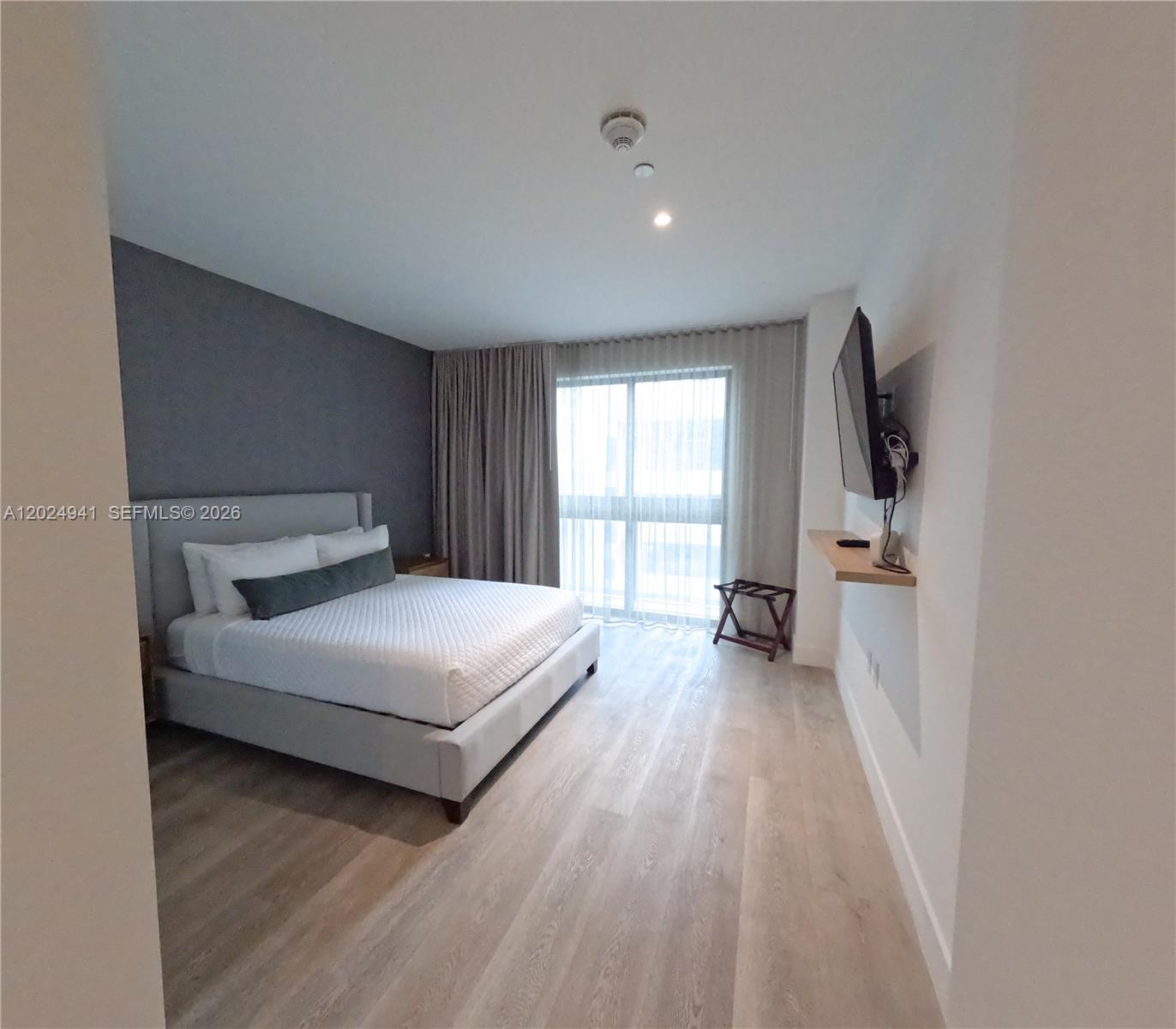 A bedroom features a gray upholstered bed, wood-look flooring, and a wall-mounted television — 229 SW 9th St # 508, Miami FL 33130, MIAMI, FL