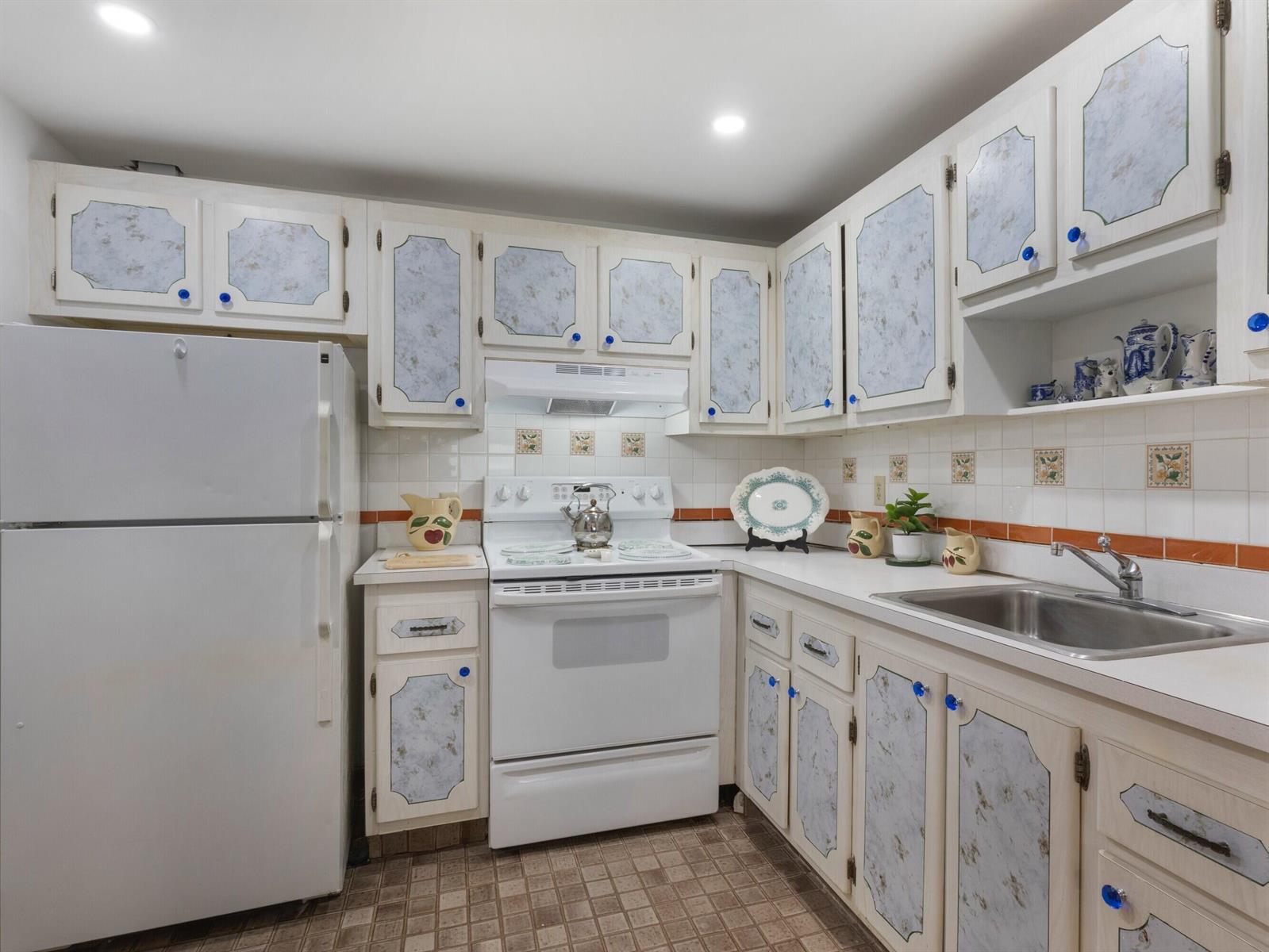 A kitchen with white cabinets featuring blue patterned panels, white appliances, and tiled countertops — 499 Saxony K, Delray Beach FL 33446, DELRAY BEACH, FL