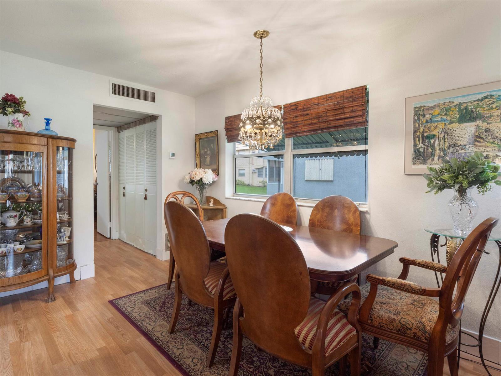 A dining room features a wooden table, matching chairs, a crystal chandelier, and a display cabinet — 499 Saxony K, Delray Beach FL 33446, DELRAY BEACH, FL