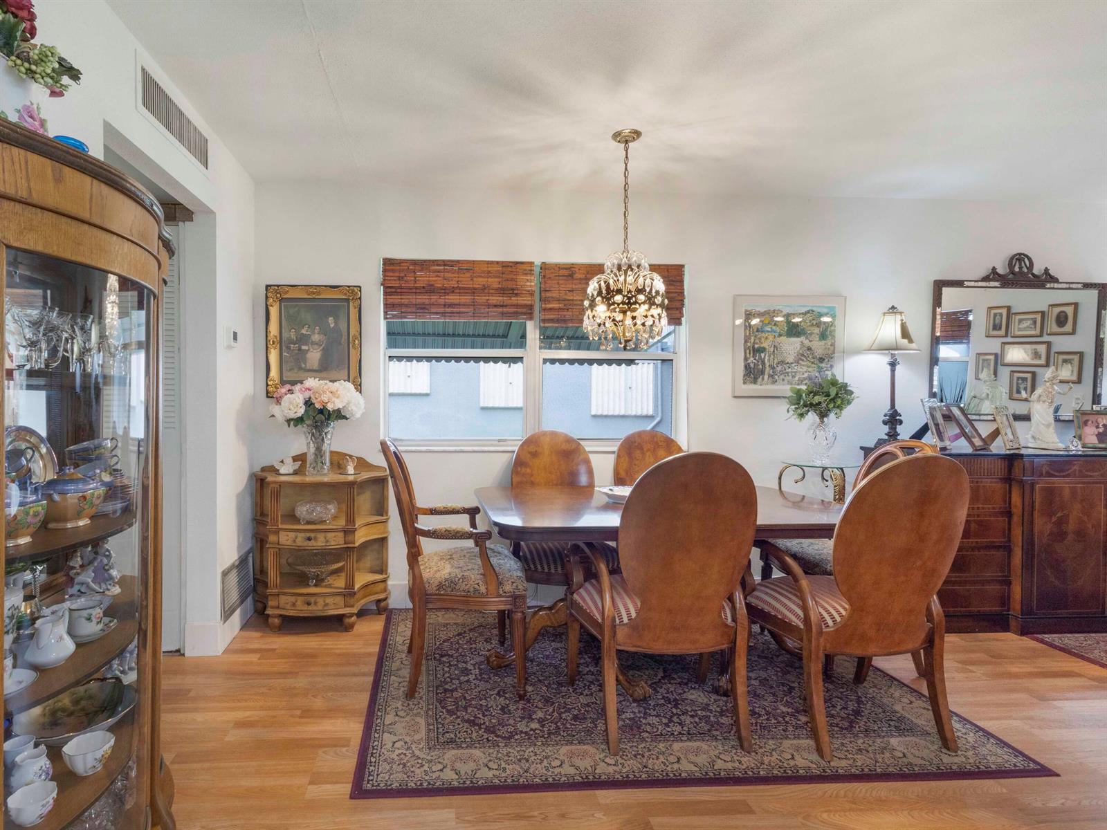 A dining room features a wooden table, six chairs, a crystal chandelier, and a display cabinet — 499 Saxony K, Delray Beach FL 33446, DELRAY BEACH, FL