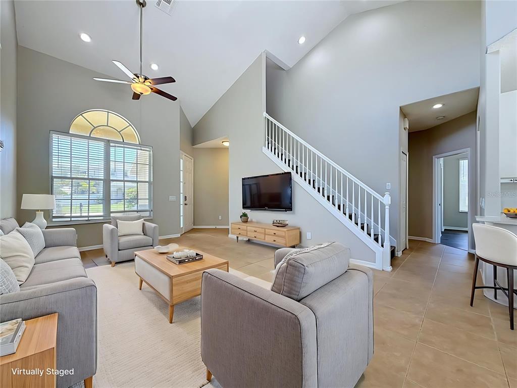 A living room with vaulted ceilings, a staircase, tile flooring, and a mounted television — 437 BRILAND STREET, TARPON SPRINGS, FL