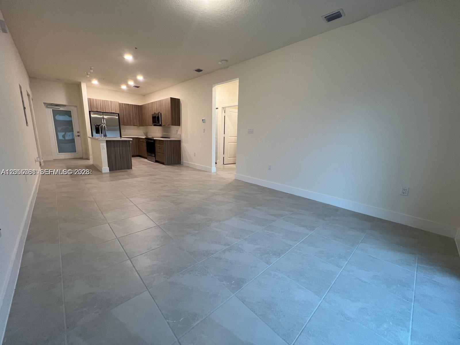An open-concept living area features light gray tile flooring and a kitchen with wood cabinets — 8363 NW 41st St # 104, Doral FL 33166, DORAL, FL