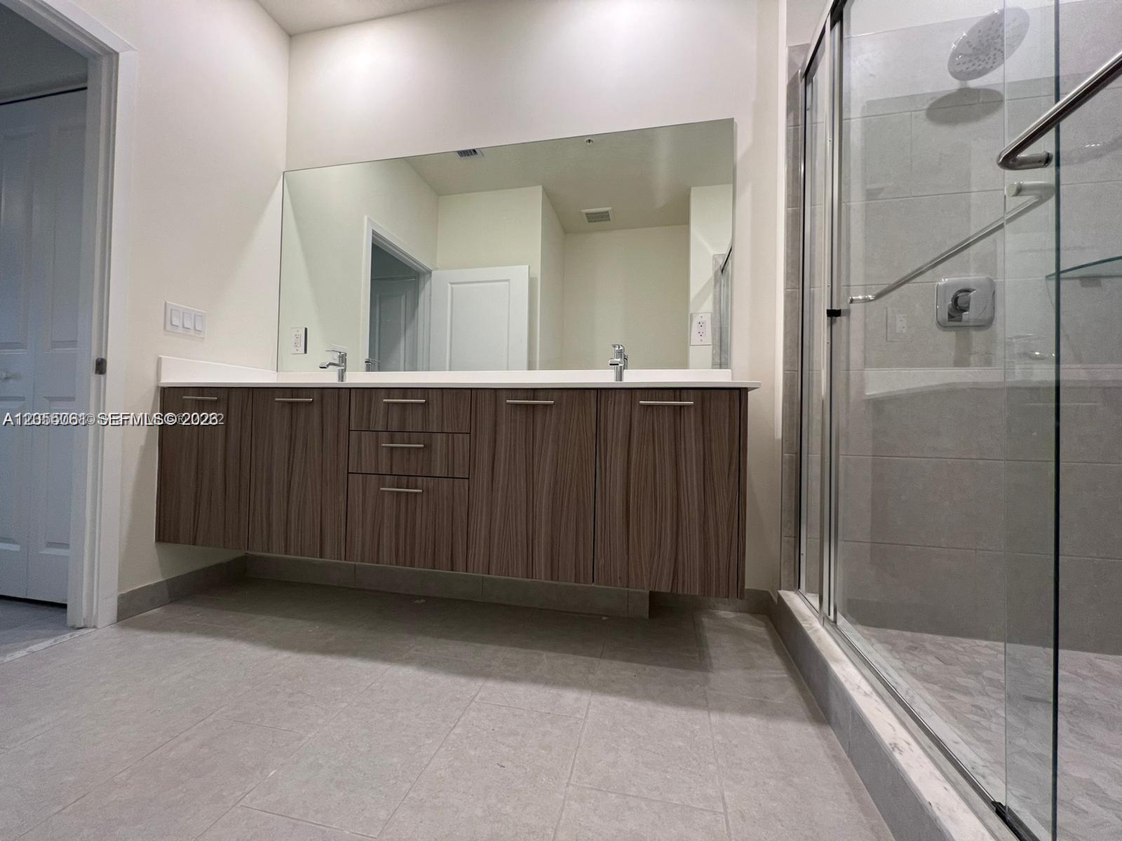 A modern bathroom features a floating wood-grain vanity with dual sinks and a glass shower — 8363 NW 41st St # 104, Doral FL 33166, DORAL, FL