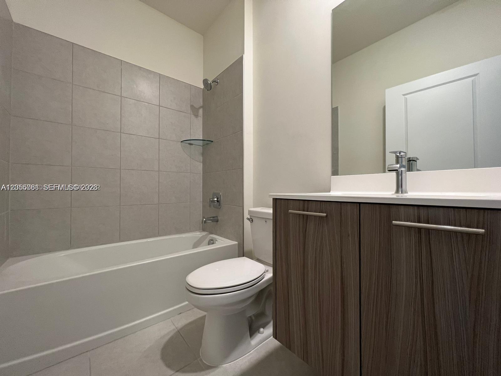 A bathroom features a tiled tub-shower combo, a white toilet, and a wood-toned vanity — 8363 NW 41st St # 104, Doral FL 33166, DORAL, FL