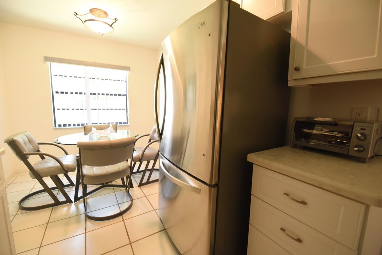 A kitchen with white cabinets, a stainless steel refrigerator, and a small dining area — 11 Southport Lane # H, Boynton Beach FL 33436, BOYNTON BEACH, FL