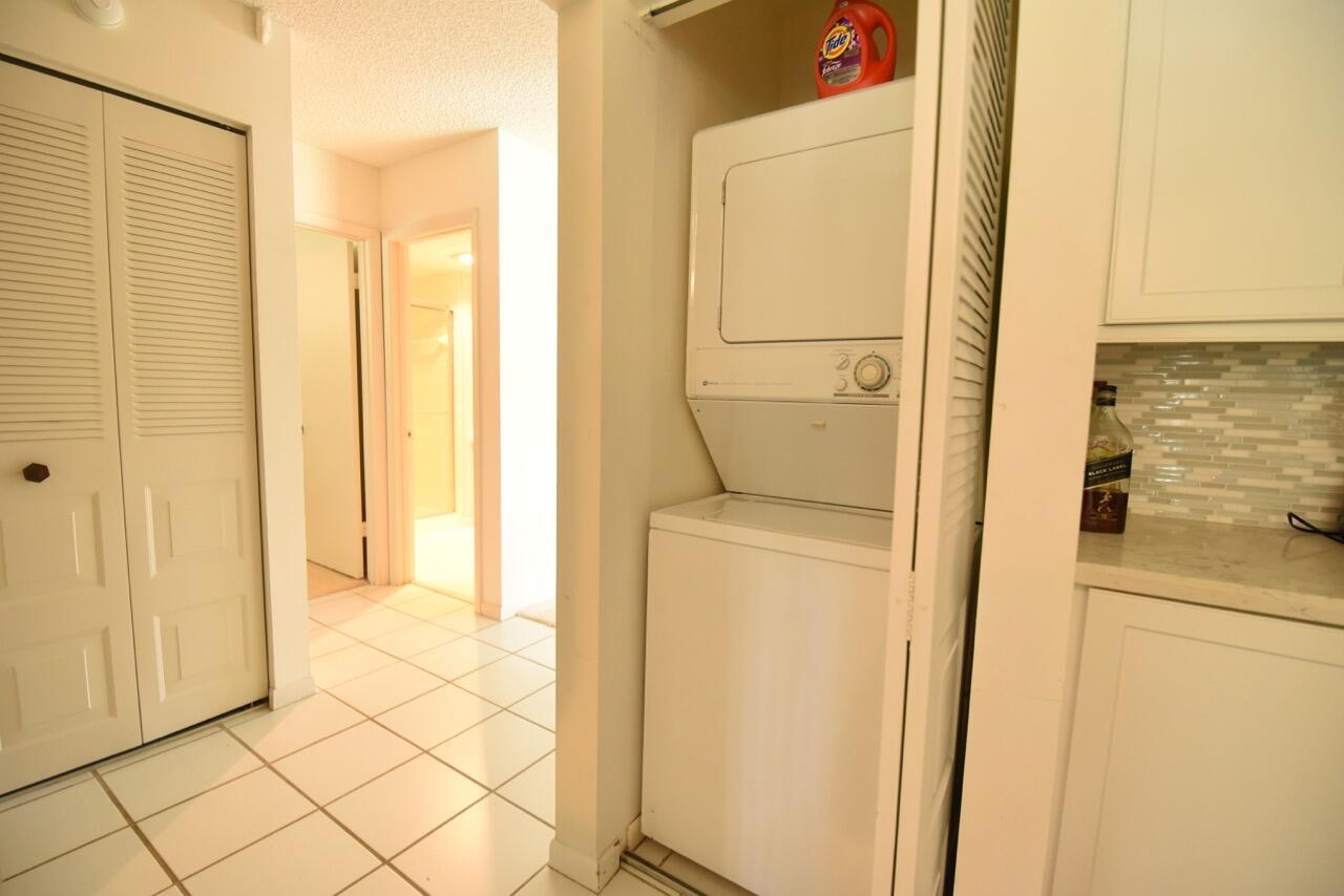 A stacked washer and dryer unit sits in a closet next to a tiled hallway — 11 Southport Lane # H, Boynton Beach FL 33436, BOYNTON BEACH, FL