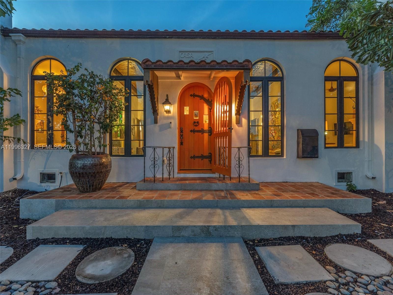 The exterior of a Spanish-style home features an arched wooden door, tiled porch, and large windows — 1321 Tyler St, Hollywood FL 33019, HOLLYWOOD, FL