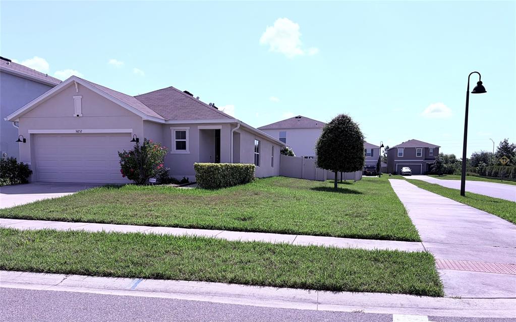 A single-story suburban house with a beige stucco exterior, a two-car garage, and a lawn — 16252 SILENT SANDS LANE, ODESSA, FL