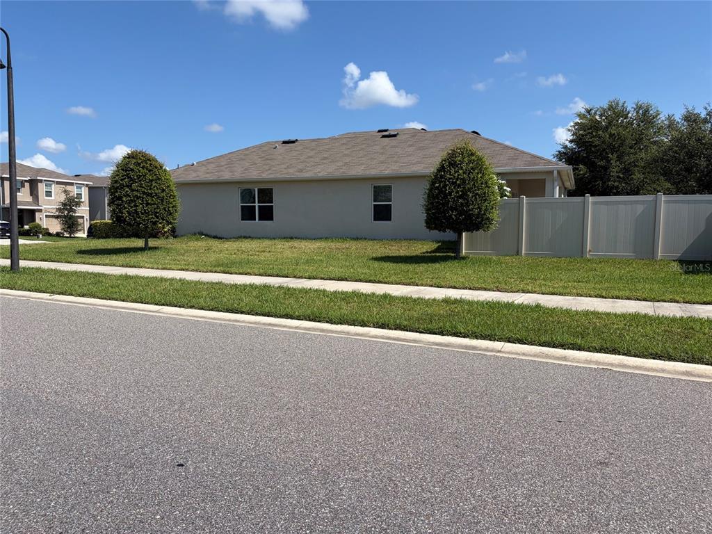 A side view of a single-story house with a lawn, two trees, and a fence — 16252 SILENT SANDS LANE, ODESSA, FL