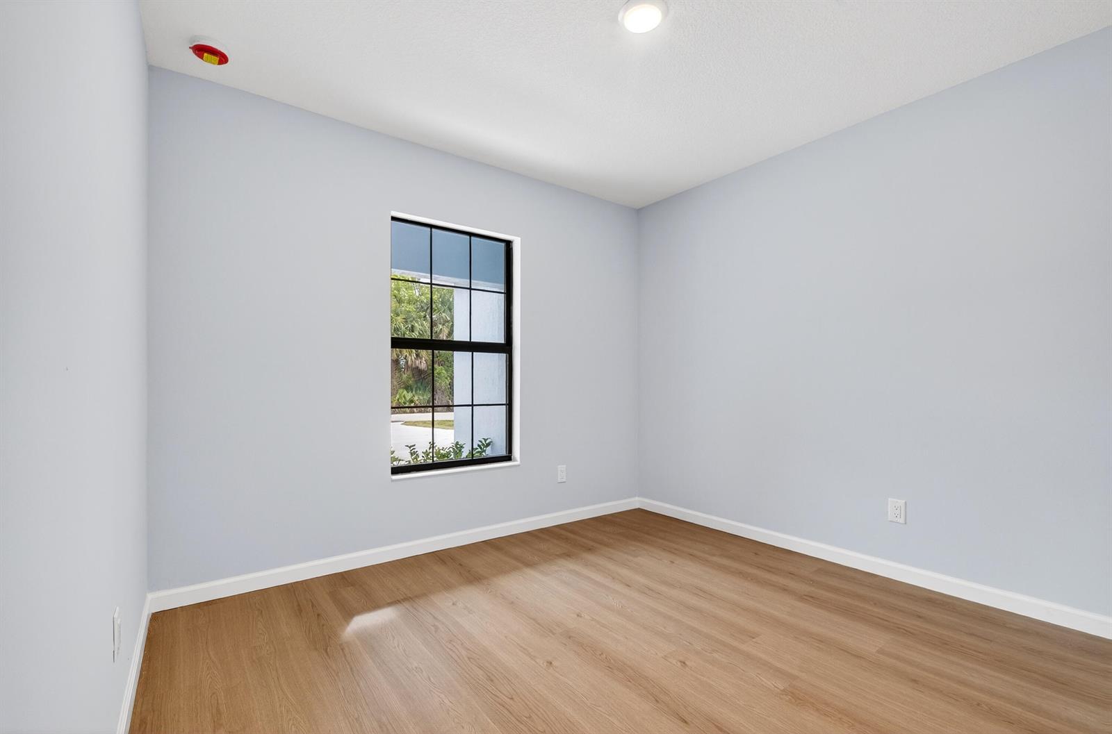 An empty room with light blue walls, wood-look flooring, and a single window — 2875 NW 32nd Avenue, Okeechobee FL 34972, OKEECHOBEE, FL