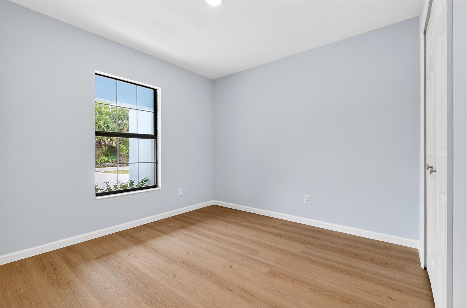 An empty room with light blue walls, wood-look flooring, and a window overlooking greenery — 2875 NW 32nd Avenue, Okeechobee FL 34972, OKEECHOBEE, FL