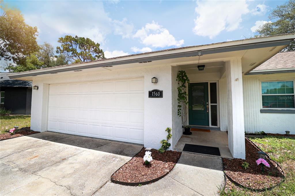 A white house exterior features a two-car garage, a green front door, and landscaping — 1560 GUINEVERE DRIVE, CASSELBERRY, FL