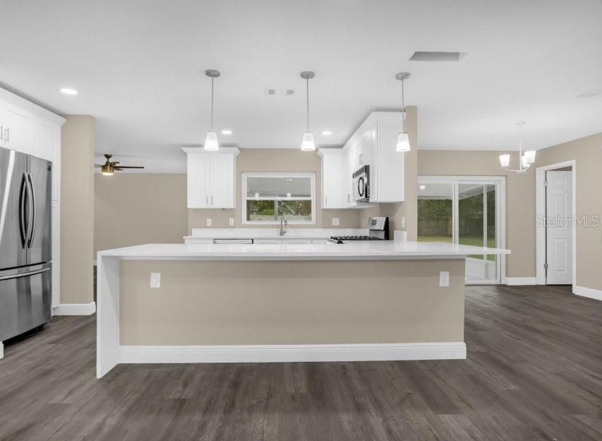 A modern kitchen features white cabinets, a large quartz island, and dark wood-look flooring — 1560 GUINEVERE DRIVE, CASSELBERRY, FL