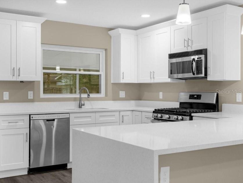A modern kitchen features white cabinets, stainless steel appliances, and a white quartz countertop island — 1560 GUINEVERE DRIVE, CASSELBERRY, FL