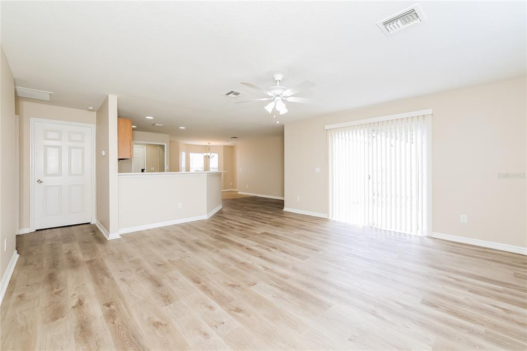A living room with light wood-look flooring, a ceiling fan, and sliding glass patio doors — 480 DANUBE DRIVE, POINCIANA, FL