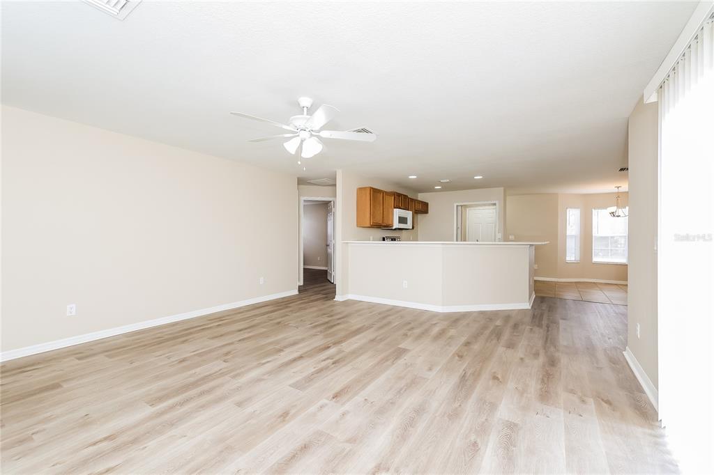 An open-concept living room features light wood-look flooring, a ceiling fan, and a kitchen peninsula — 480 DANUBE DRIVE, POINCIANA, FL