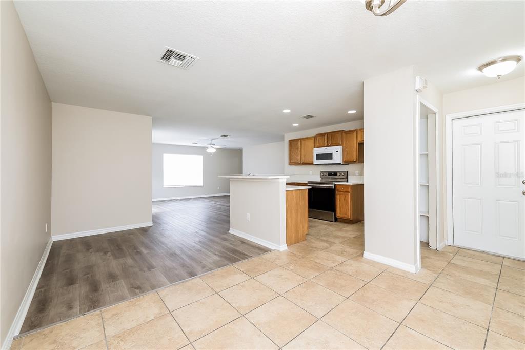An open-concept kitchen with wood cabinets and tile floors transitions into a wood-floored living area — 480 DANUBE DRIVE, POINCIANA, FL