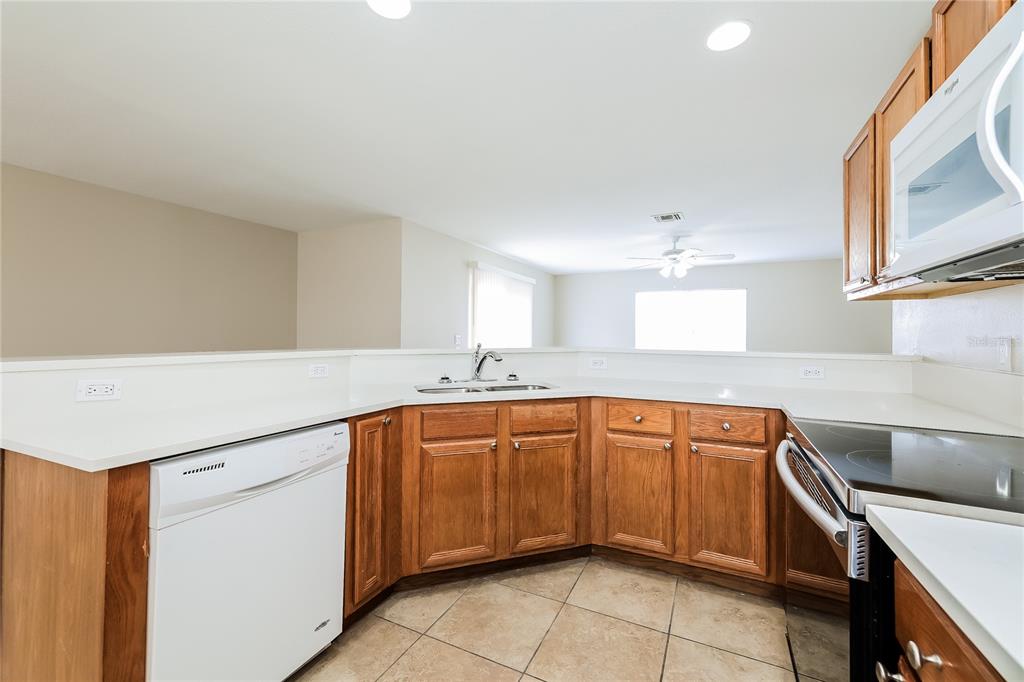 A kitchen features wood cabinets, white countertops, a white dishwasher, and tile flooring — 480 DANUBE DRIVE, POINCIANA, FL