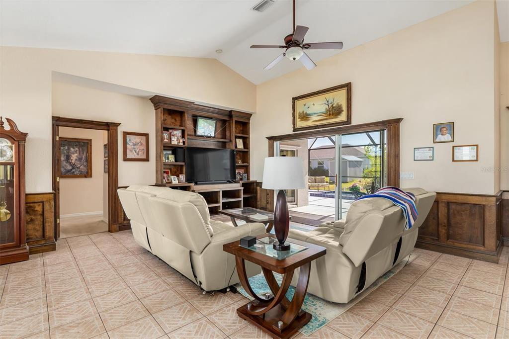 A living room features tile floors, a vaulted ceiling, a built-in entertainment center, and sliding doors — 10056 LEBANON DRIVE, PORT CHARLOTTE, FL