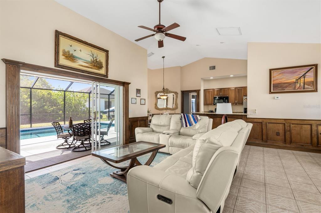 A living room with light-colored sofas, wood wainscoting, and sliding doors opening to a pool — 10056 LEBANON DRIVE, PORT CHARLOTTE, FL