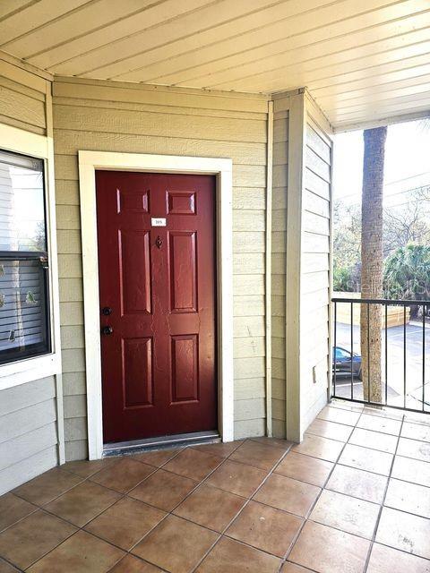 A red front door with a number plate sits on a tiled porch with beige siding — 3020 PARKWAY BOULEVARD UNIT 203, KISSIMMEE, FL