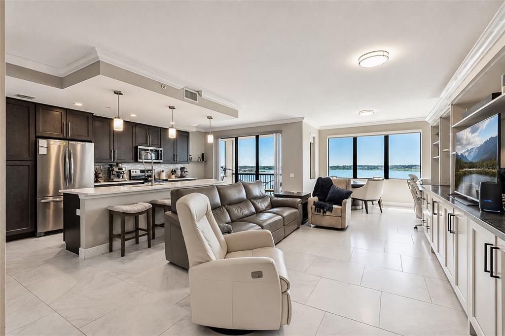 An open-concept living room and kitchen with white tile floors, dark cabinetry, and water views — 16300 COUNTY ROAD 455 UNIT 511, MONTVERDE, FL