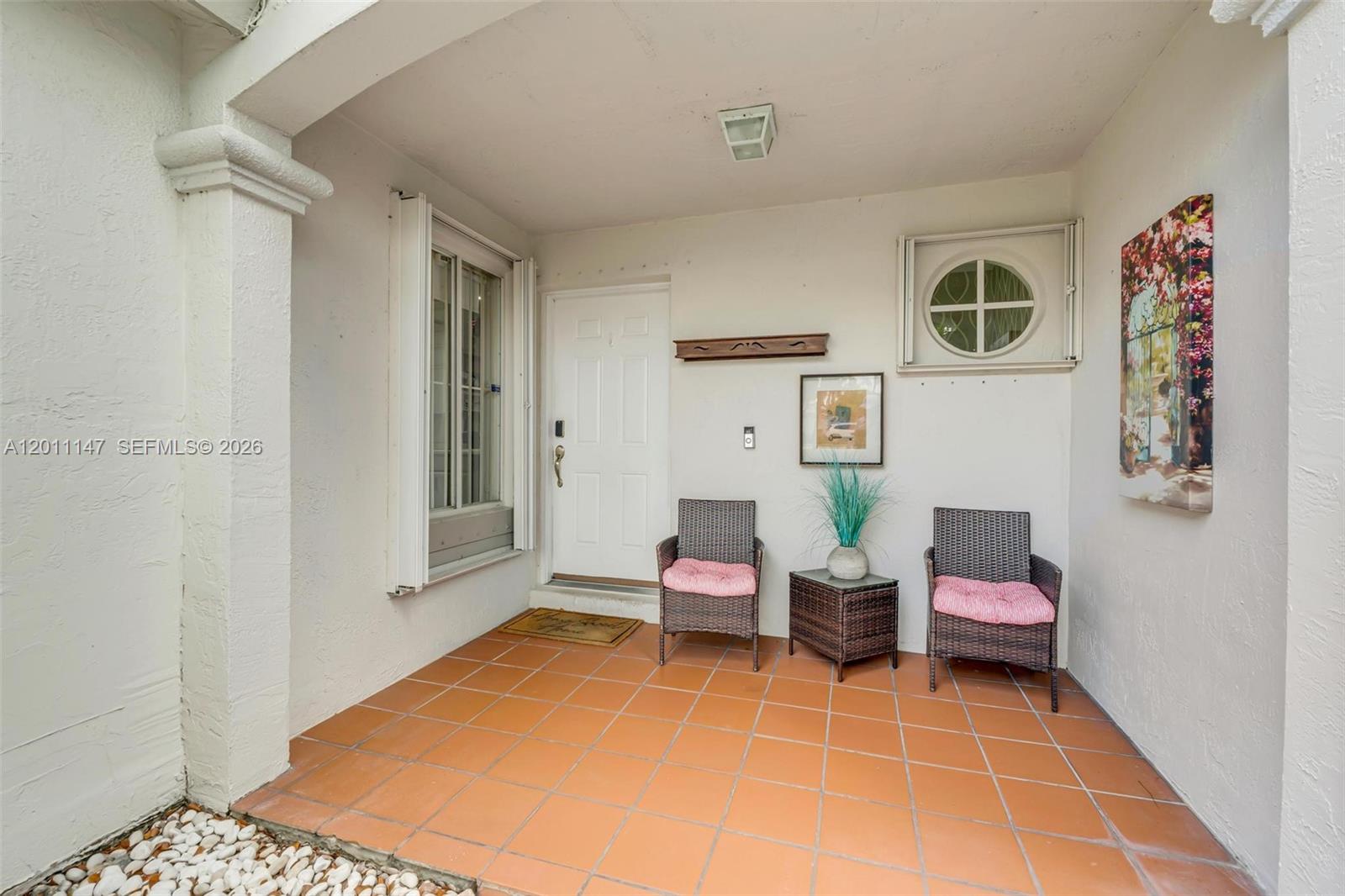 A covered patio features terracotta tile flooring, two wicker chairs, and a white front door — 16221 SW 72nd Ter, Miami FL 33193, MIAMI, FL