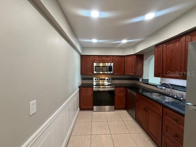 A kitchen features cherry wood cabinets, stainless steel appliances, and light-colored tile flooring — 700 MIRROR TERRACE NW UNIT 507, WINTER HAVEN, FL