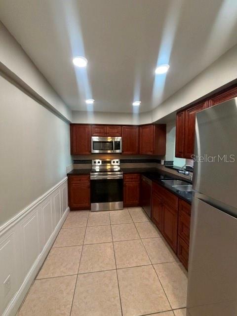 A galley kitchen features wood cabinets, stainless steel appliances, and light-colored tile flooring — 700 MIRROR TERRACE NW UNIT 507, WINTER HAVEN, FL