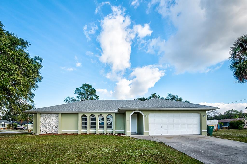 A single-story house with light green siding, a white garage door, and a stone accent wall — 504 VANNELL STREET, PORT CHARLOTTE, FL