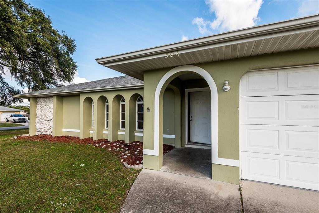 The exterior of a green house features an arched entryway and a white garage door — 504 VANNELL STREET, PORT CHARLOTTE, FL