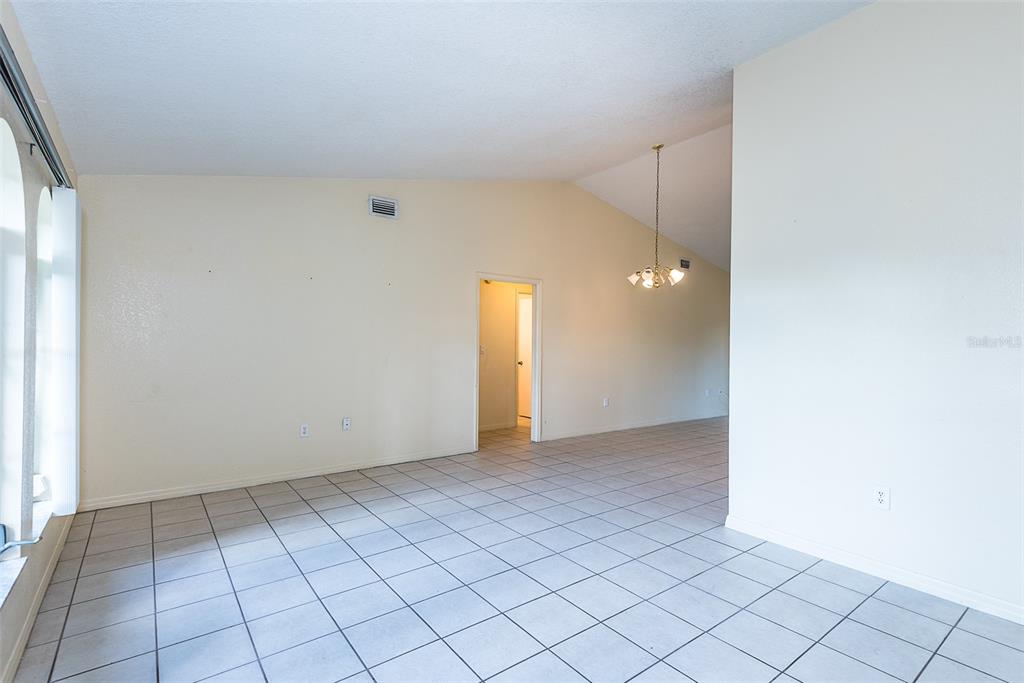 An empty room with light-colored tile flooring, vaulted ceilings, and a central doorway — 504 VANNELL STREET, PORT CHARLOTTE, FL