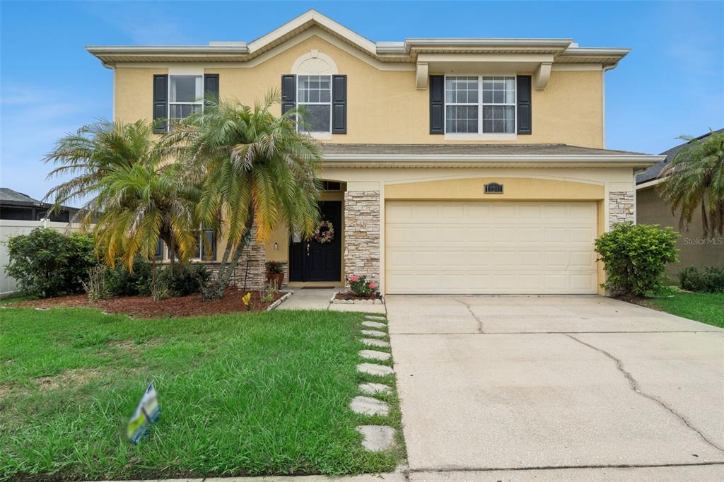 A two-story house with a beige stucco exterior, stone accents, and a two-car garage — 12202 ACCIPITER DRIVE, ORLANDO, FL