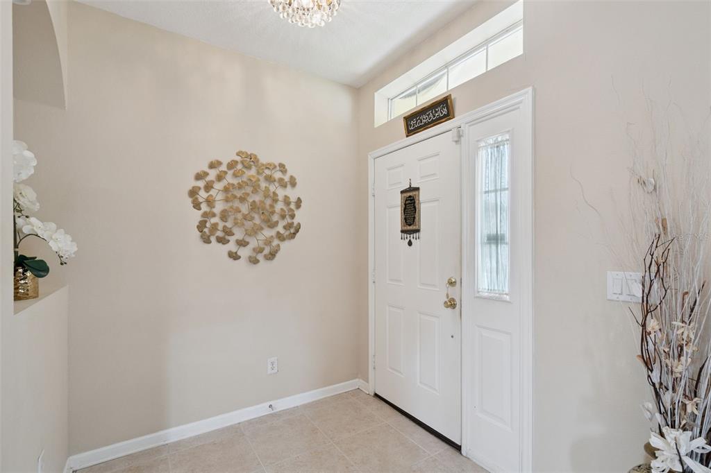 An entryway features a white front door, tile flooring, and gold wall art — 12202 ACCIPITER DRIVE, ORLANDO, FL