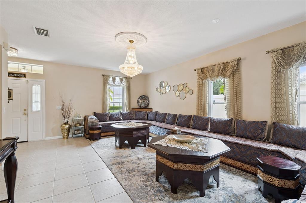 A living room features a large sectional sofa, two hexagonal coffee tables, and a crystal chandelier — 12202 ACCIPITER DRIVE, ORLANDO, FL