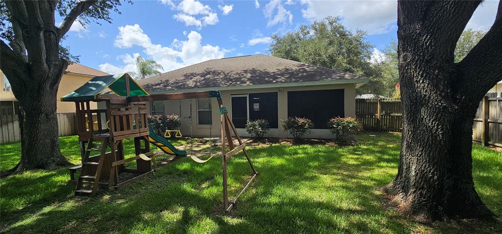 A backyard features a wooden playset, large trees, and a screened-in patio on the house — 1068 VANDERBILT DRIVE, EUSTIS, FL