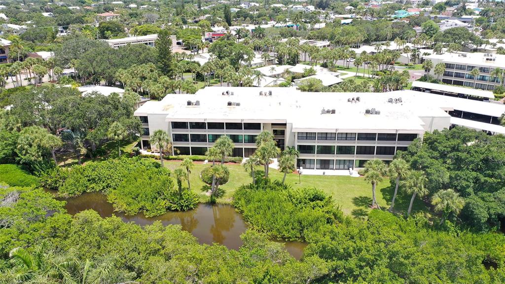 An aerial view shows a multi-story apartment building surrounded by lush trees and a pond — 225 HOURGLASS WAY UNIT 103, SARASOTA, FL