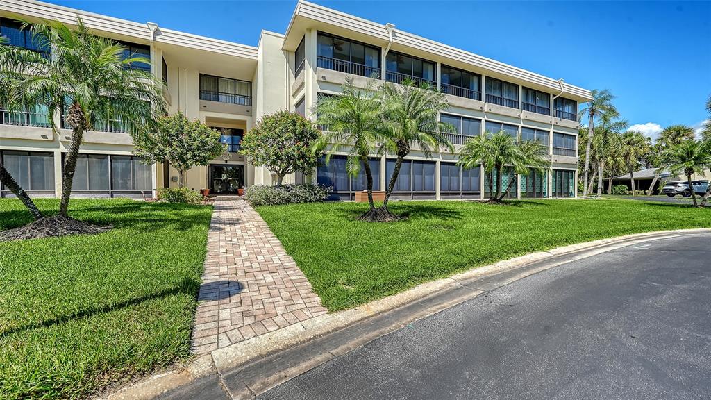 A three-story apartment building with screened balconies, palm trees, and a brick walkway — 225 HOURGLASS WAY UNIT 103, SARASOTA, FL