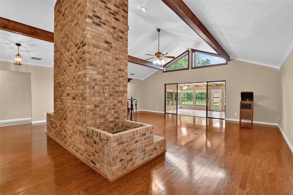 A spacious living room features a large brick fireplace, vaulted ceilings with exposed beams, and hardwood floors — 815 LAKE NED ROAD, WINTER HAVEN, FL