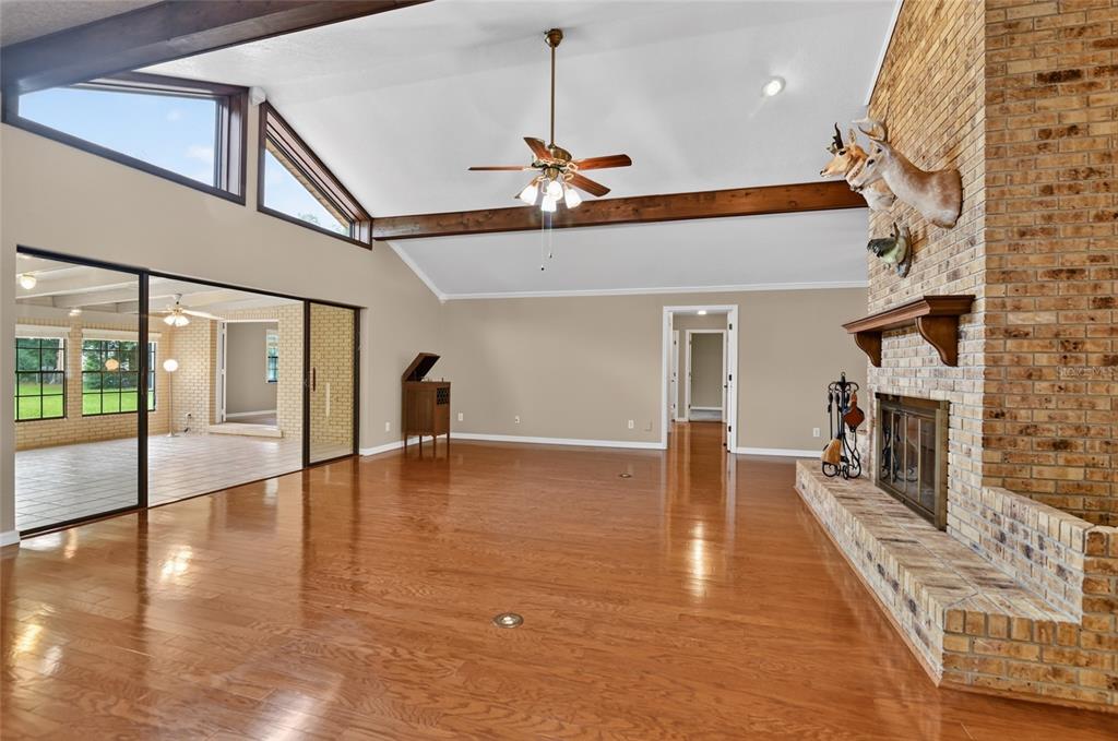 A spacious living room features hardwood floors, a vaulted ceiling with beams, and a brick fireplace — 815 LAKE NED ROAD, WINTER HAVEN, FL