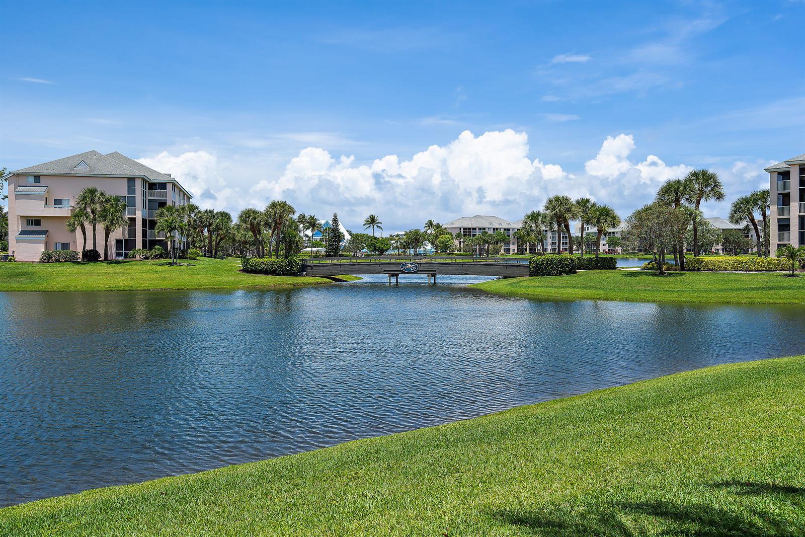 A bridge crosses a pond between multi-story apartment buildings surrounded by palm trees and grass — 353 S Us Hwy 1 # A8, Jupiter FL 33477, JUPITER, FL