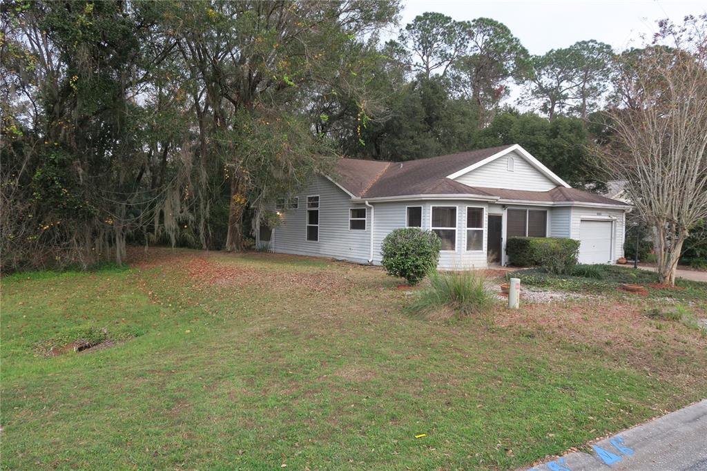 A single-story house with light gray siding and a garage sits on a grassy lot — 32512 OAK PARK DRIVE, LEESBURG, FL