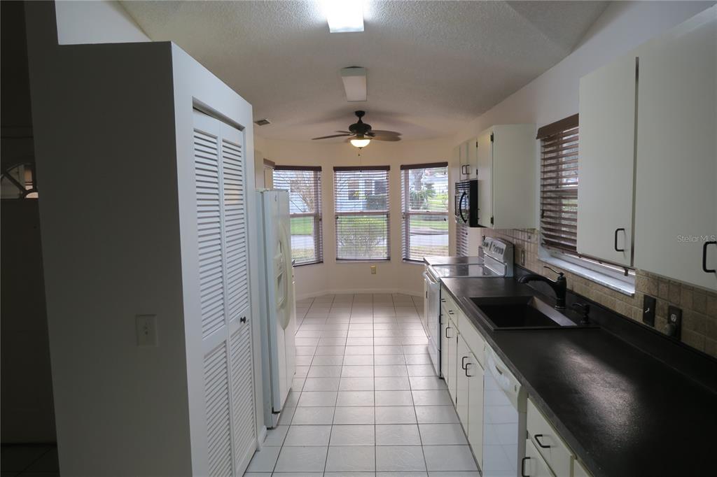 A galley kitchen features white cabinets, black countertops, tiled flooring, and a breakfast nook area — 32512 OAK PARK DRIVE, LEESBURG, FL