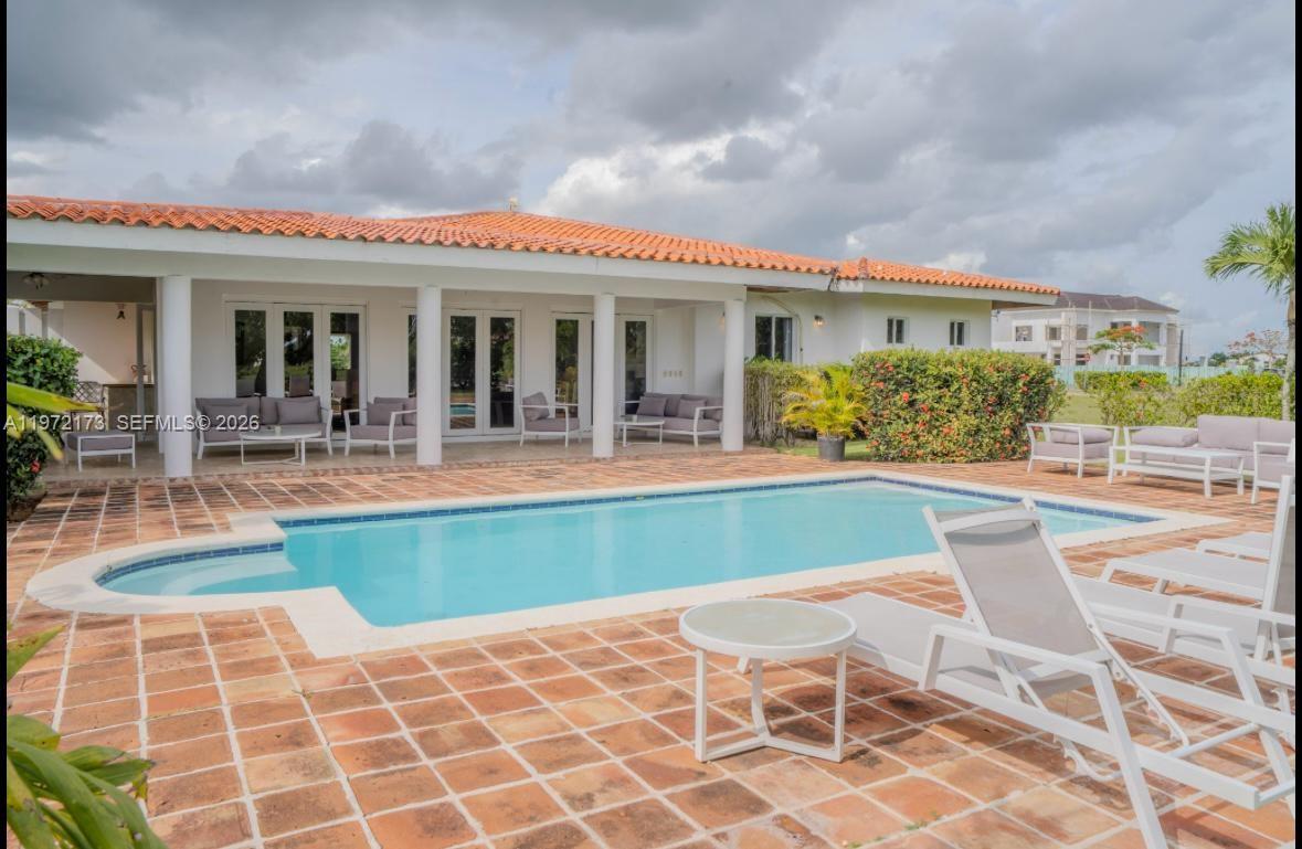 A backyard features a rectangular swimming pool surrounded by a terracotta tiled patio and furniture — Los Samanes La Estancia, DR 0, DR