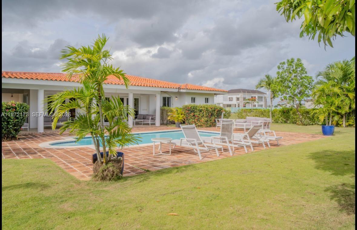 A swimming pool with lounge chairs sits on a brick patio behind a one-story house — Los Samanes La Estancia, DR 0, DR