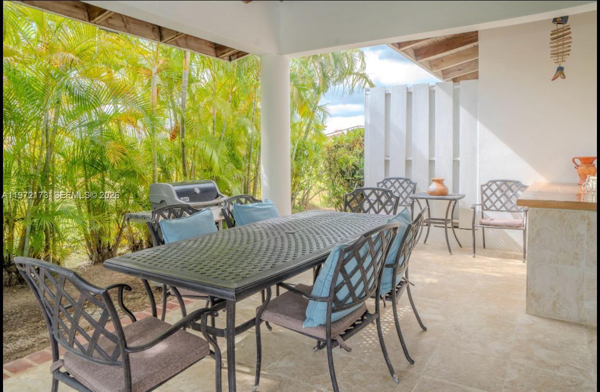 A covered outdoor patio features a dining table with chairs and a grill near palm trees — Los Samanes La Estancia, DR 0, DR